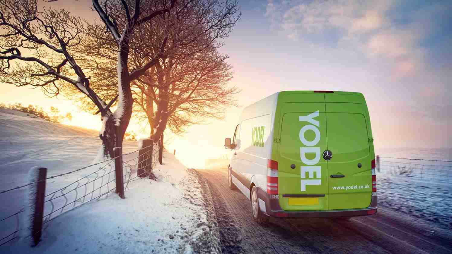 A green Yodel delivery van drives on a snowy rural road at sunset, with snow-covered trees and fields lining the path.